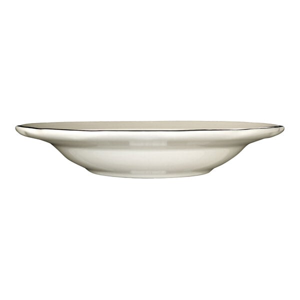 A deep rim stoneware soup bowl in ivory with a scalloped edge and a black rim.