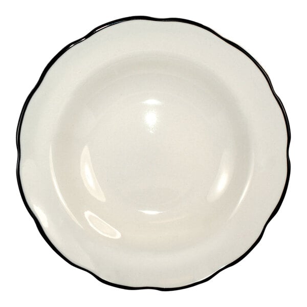 A deep rim stoneware soup bowl in ivory with a scalloped edge and a black rim.