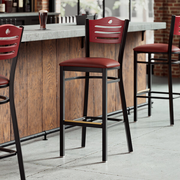 A row of Lancaster Table & Seating bar stools with mahogany wood backs and burgundy cushions at a bar counter.