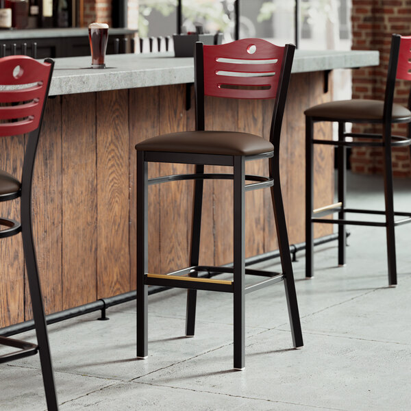 A row of Lancaster Table & Seating black bar stools with mahogany wood backs and dark brown vinyl seats at a bar counter.