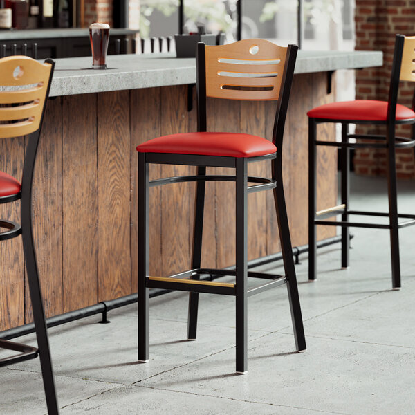 A row of Lancaster Table & Seating bar stools with red vinyl seats and natural wood backs.