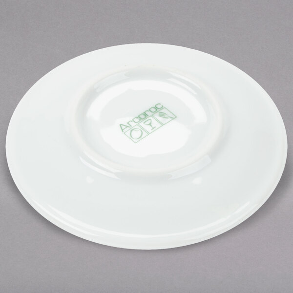 An Arcoroc white saucer with green writing on it.