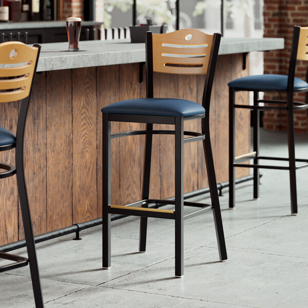 Three Lancaster Table & Seating restaurant bar stools with navy vinyl seats and natural wood backs at a counter.