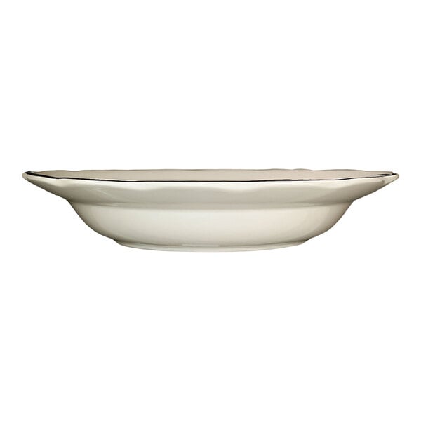 A scalloped edge ivory stoneware pasta bowl with a black rim.