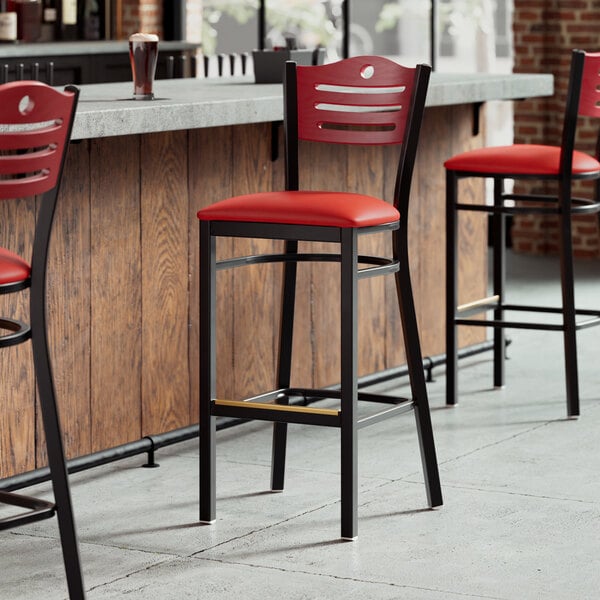 A row of Lancaster Table & Seating black bar stools with red vinyl seats and mahogany backs.
