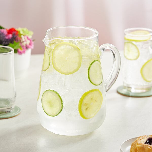 An Acopa round glass pitcher of water with lemon slices and ice.