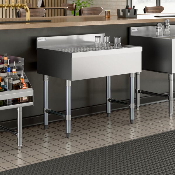 A stainless steel underbar drainboard with a grated top and four legs, designed for bar use.