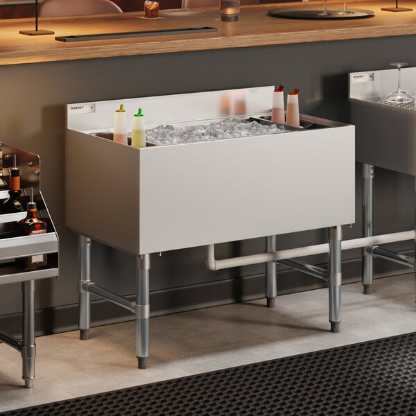 A stainless steel underbar ice bin with a cold plate and bottle holders, filled with ice and condiment bottles, designed for bar use.