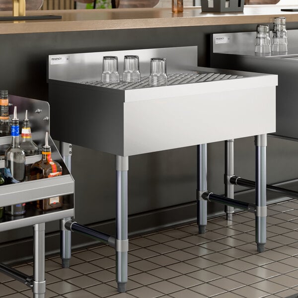 A stainless steel underbar drainboard with a grated surface and four legs, designed for commercial bar use.