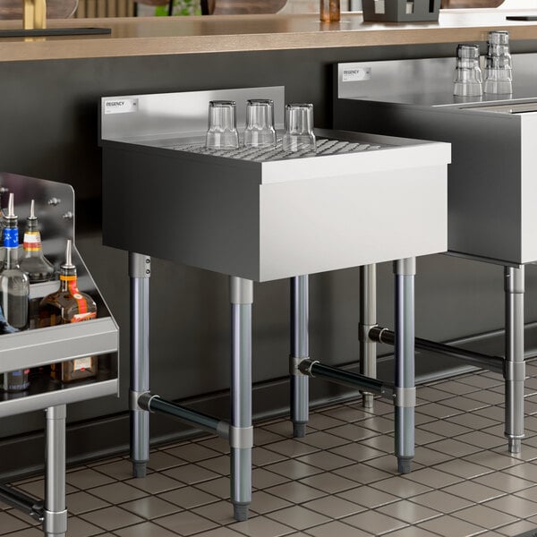 A stainless steel underbar drainboard with a grated top and several glasses placed upside down.