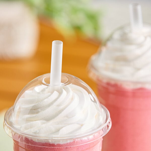 A translucent, pointed, unwrapped smoothie straw inserted into a pink smoothie with whipped cream in a clear plastic cup.