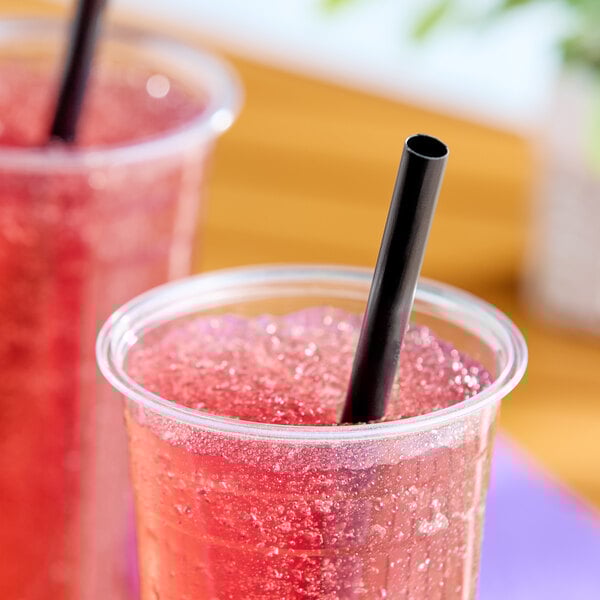 A black pointed unwrapped smoothie straw placed in a clear plastic cup filled with a red slushy beverage.