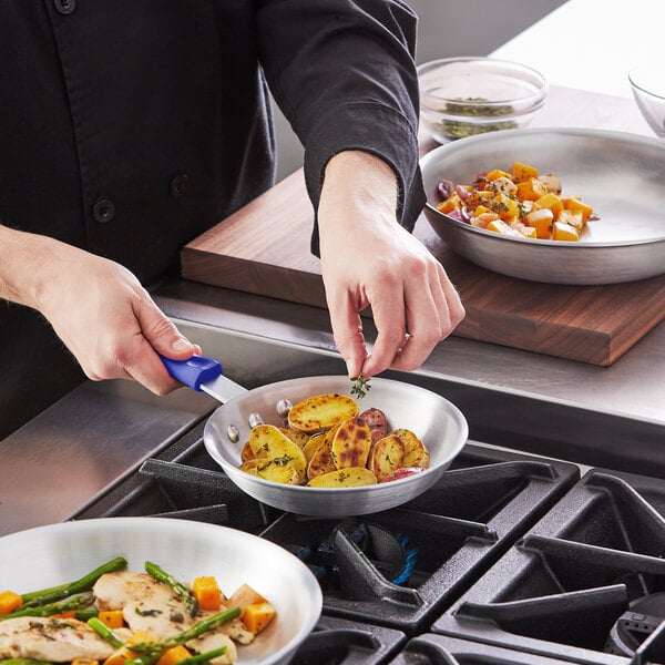 A person cooking meat and vegetables in a Choice aluminum fry pan.