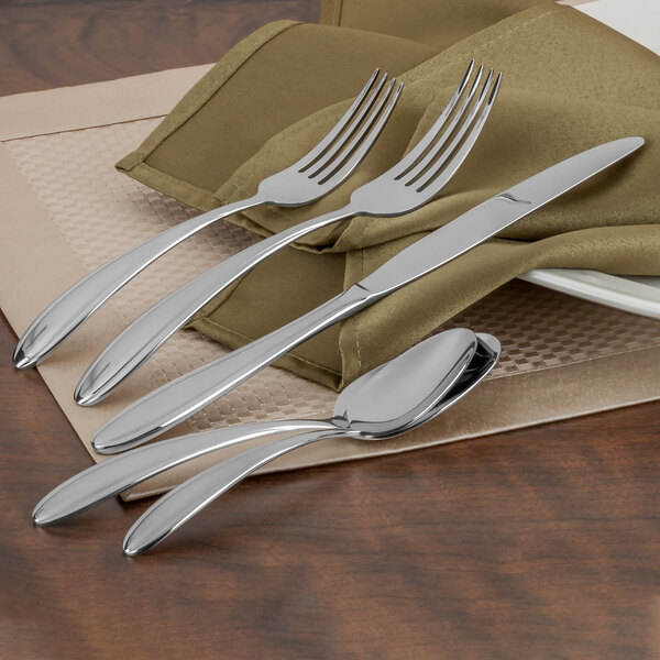 A Walco stainless steel dessert spoon on a white napkin with other silverware.