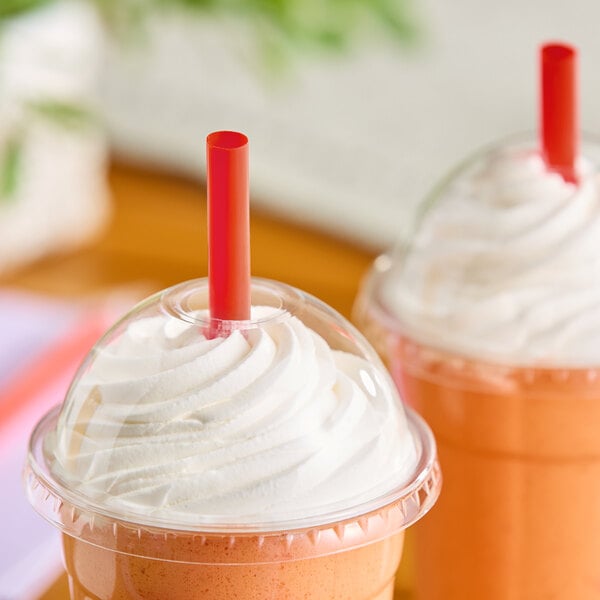 A red pointed smoothie straw inserted into a plastic cup with a dome lid and whipped topping.