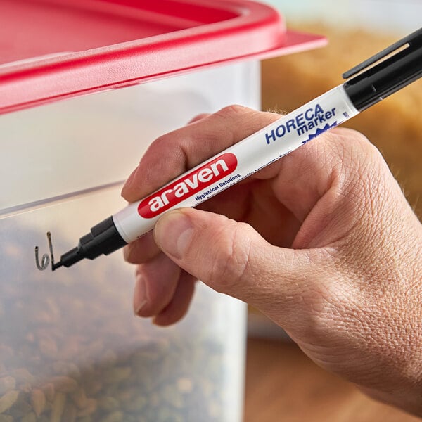 A hand using a black Araven marker to write on a container.