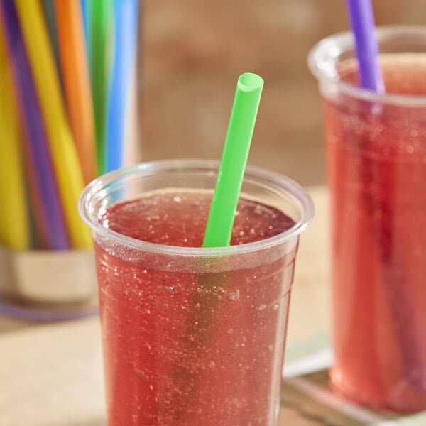 A clear plastic cup filled with a red beverage and a green neon pointed smoothie straw.