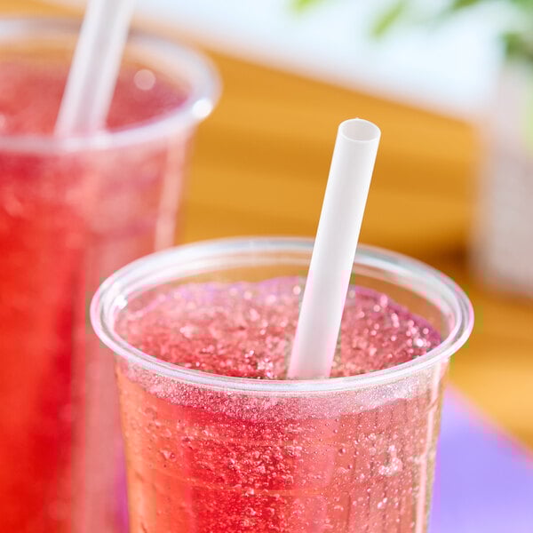 A clear plastic cup filled with a red beverage and a translucent pointed unwrapped smoothie straw.