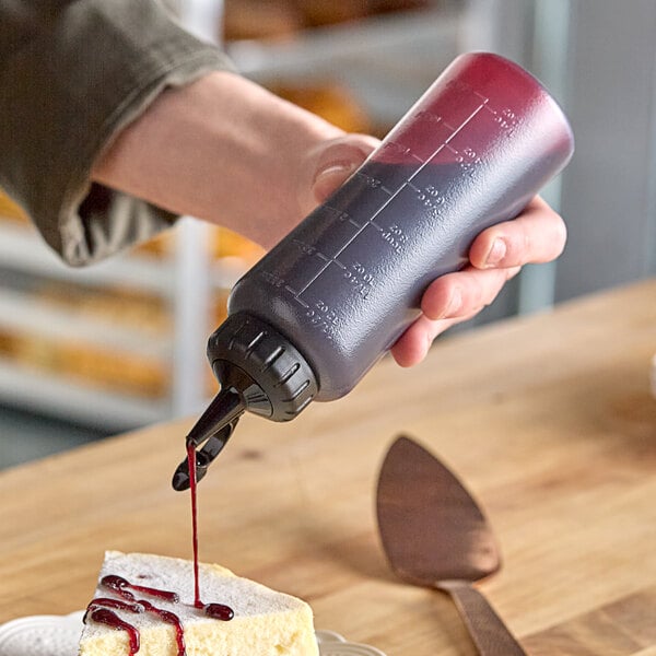 A person using an OXO squeeze bottle to pour red liquid onto food.
