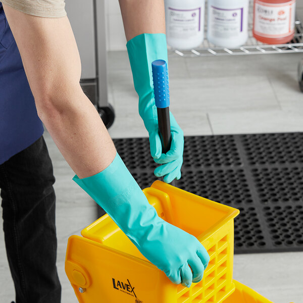 A person in green Cordova nitrile gloves holding a yellow container.