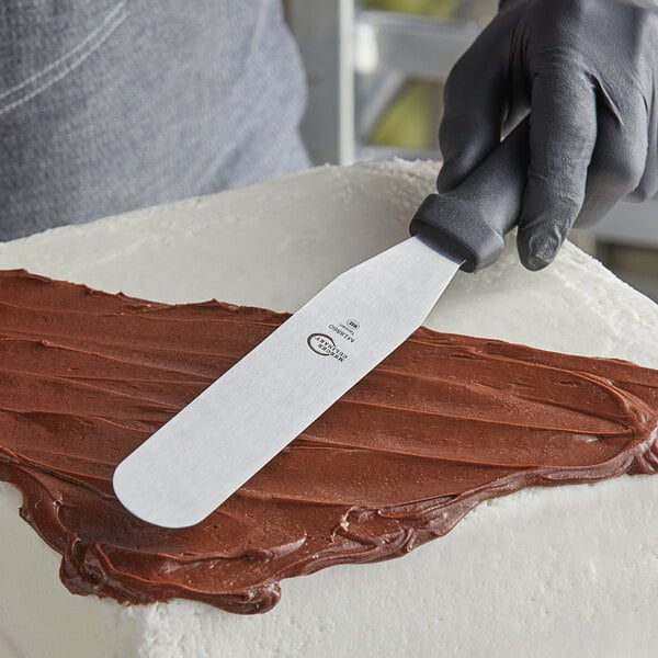 A person using a Mercer Culinary straight baking spatula to frost a brown cake.