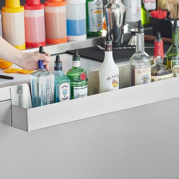 A person using a Regency stainless steel speed rail to hold bottles of alcohol on a counter.