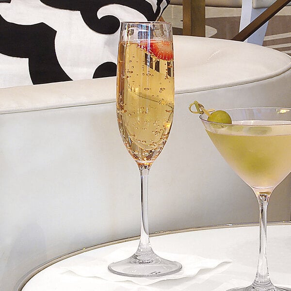 Two Front of the House Drinkwise Tritan plastic champagne flutes filled with champagne next to a martini glass.
