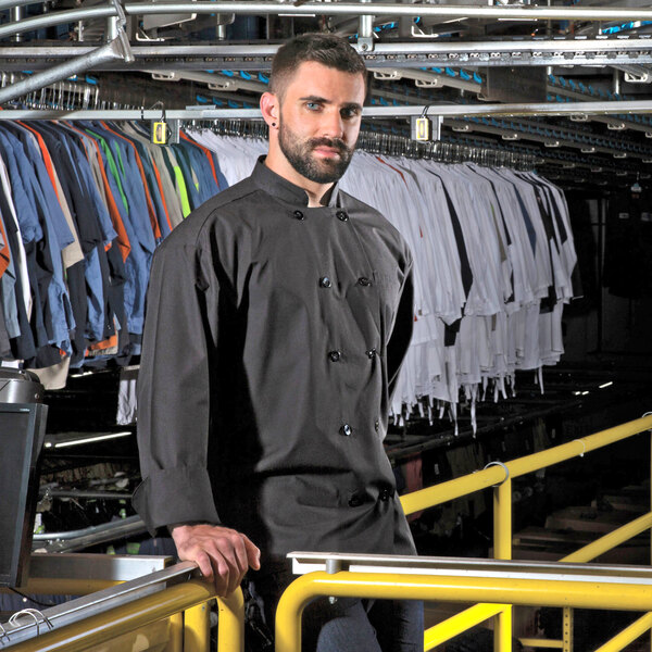 A man wearing a black Uncommon Chef long sleeve chef coat with 10 buttons.