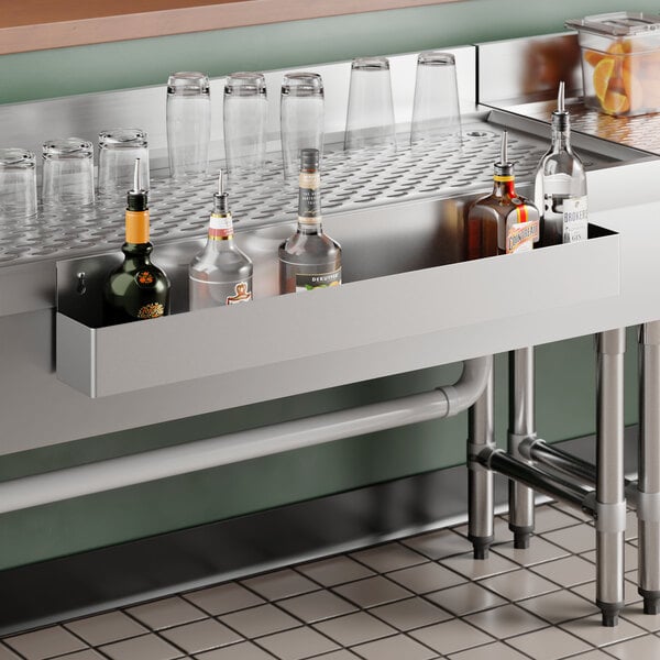 A 36-inch Steelton stainless steel single tier speed rail mounted below a bar counter holding several liquor bottles.