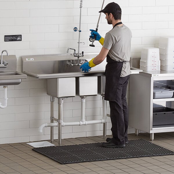 A man in yellow gloves washing a Regency 3 compartment sink.