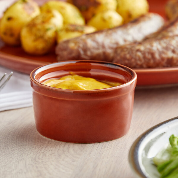 A bowl of mustard in front of a plate of food.