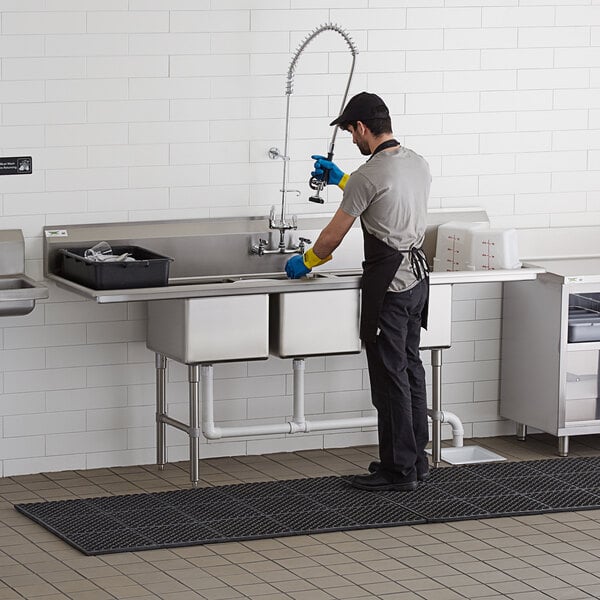 A man cleaning a Regency stainless steel 3 compartment sink in a kitchen.