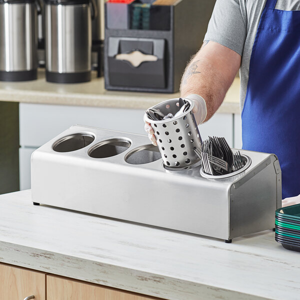 A man in a blue apron holding a Steril-Sil stainless steel flatware organizer filled with utensils.