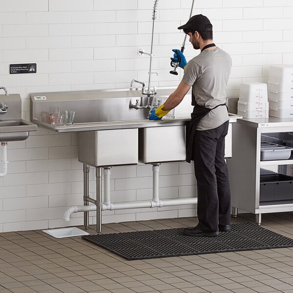 A man washing dishes in a Regency stainless steel three compartment sink.