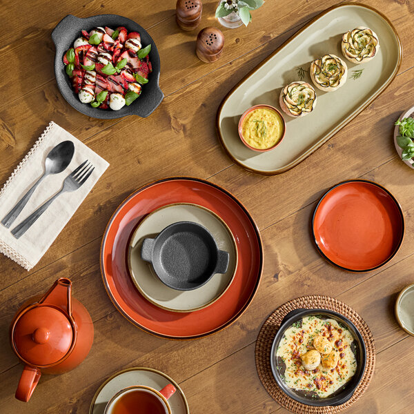 A set of two granite gray stoneware creamers placed on a wooden table among various dishes and tableware.