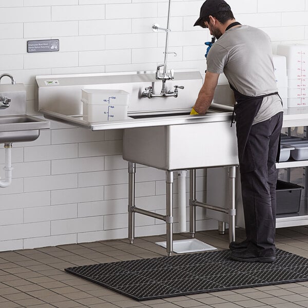 A man washing a Regency stainless steel sink in a professional kitchen.