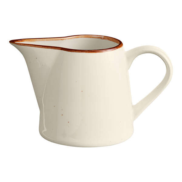 A small vanilla-colored porcelain creamer with a handle and a brown rim.