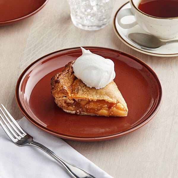 A plate of pie with a fork and spoon on a table with a cup of tea.