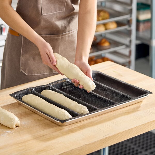 A five-compartment silicone bread mold for making sub sandwich loaves, shown with dough being placed into the mold.