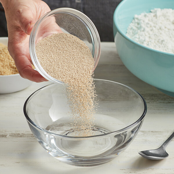 A person pouring Lesaffre SAF-Instant Red Dry Yeast into a bowl of flour.