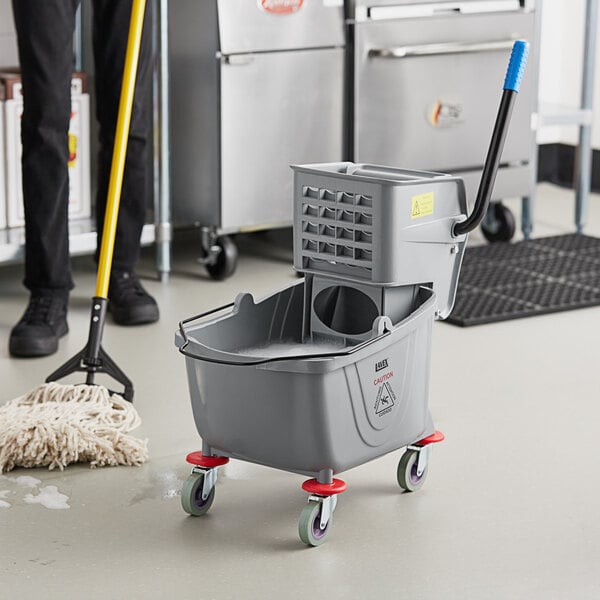 A man using a Lavex mop and bucket to clean a floor in a school kitchen.