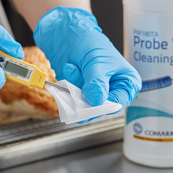 A person wearing blue gloves using a Comark thermometer to wipe a meat thermometer with a Comark probe wipe.