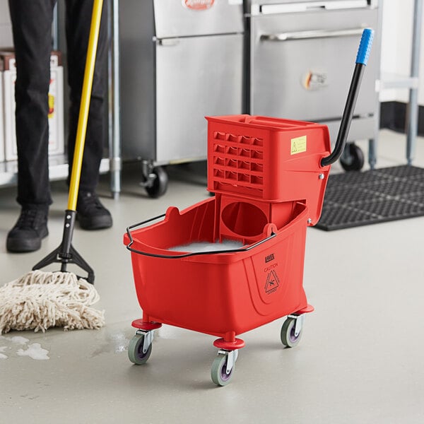 A man using a Lavex red mop bucket to clean the floor in a school kitchen.