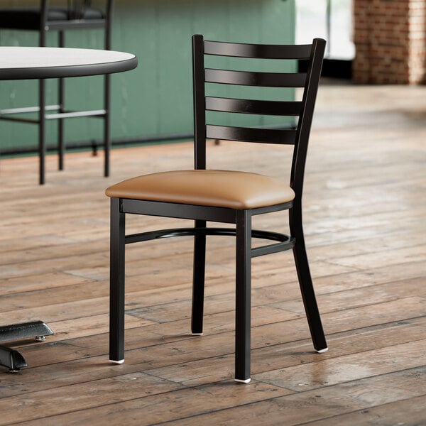 A Lancaster Table & Seating black ladder back chair with light brown vinyl padded seat.