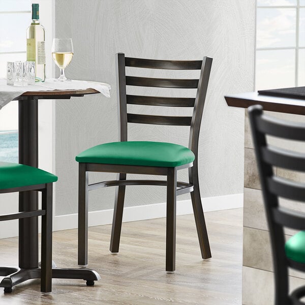 A Lancaster Table & Seating distressed copper ladder back chair with a green vinyl cushion on it at a restaurant table with wine glasses and bottles.