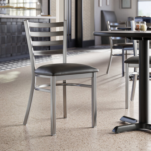 A Lancaster Table & Seating ladder back chair with a black vinyl padded seat.