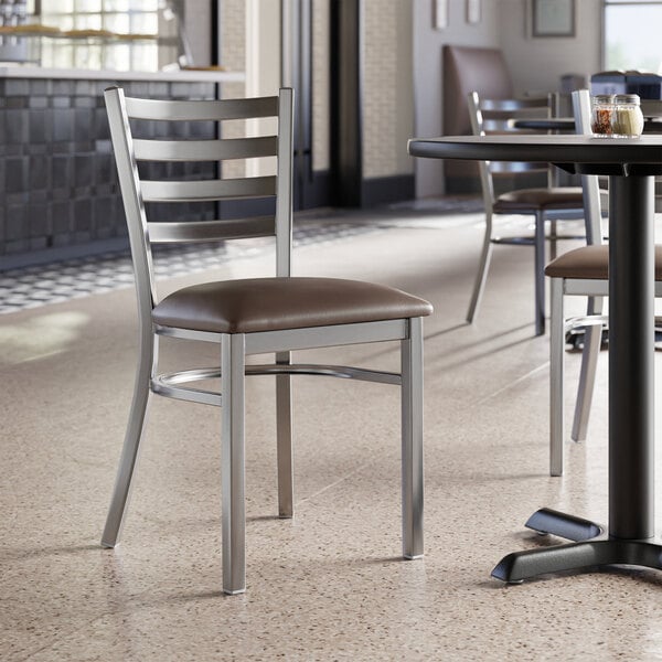 A Lancaster Table & Seating ladder back chair with a dark brown vinyl padded seat on a table in a restaurant.