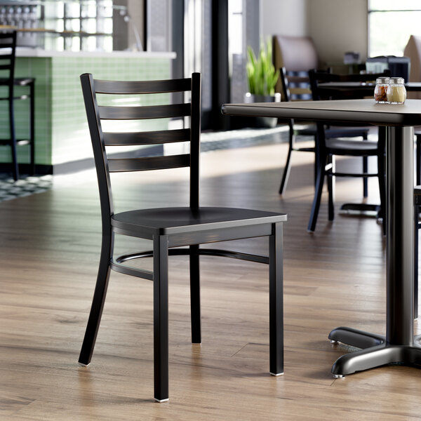 A black ladder back chair with a black wood seat and a distressed copper finish, shown in a restaurant setting.