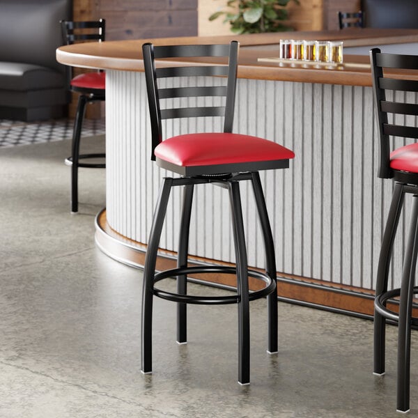 A black ladder back swivel bar stool with a red vinyl padded seat.