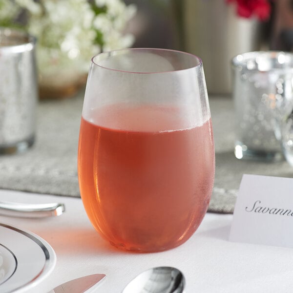 A Visions clear plastic stemless wine glass filled with pink liquid on a table.